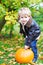 Little toddler kid boy with big orange pumpkin in autumn garden. cute child in fashion clothes having fun with huge