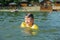 Little toddler kid swimming in lake with inflatable arms aids support