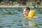 Little toddler kid swimming in lake with inflatable arms aids support