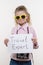 Little tourist specialist, child girl with a photo camera in sunglasses holding white sheet of paper with the text Travel expert,