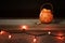 Little Trick or Treat Halloween Pumpkin filled with candy corn on a rustic wood shelf with row of orange lights and dark backgroun