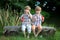 Little Twin Brothers Sitting on Wooden Bench and Blowing Soap Bubbles in Summer Park