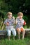 Little Twin Brothers Sitting on Wooden Bench and Blowing Soap Bubbles in Summer Park