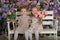 Little twin girls in the garden on a bench against the background of a floral wall with bouquets of flowers in their hands