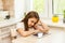 Little Upset girl at home in the kitchen sitting at the table with tablet