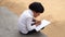 Little village girl doing homework in notebook and sitting on stone near goat farm. Indian countryside footage