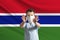 Little white boy in a protective mask on the background of the flag of Gambia. Makes a stop sign with his hands, stay at home