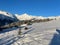 little wooden cabins in a snow covered meadow with white mountains in the background on a sunny day