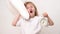 A little yawning girl hugs a pillow and an alarm clock on a white background.