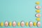 Little yellow Easter eggs arranged alternately in a line with Easter candies designed as egg white with yolk on an aqua menthe