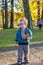 Little young boy with glasses goes in a park and hold a leaf in hand