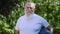 Live camera approaches to smiling senior bearded man posing with exercise mat outdoors. Zoom in portrait of motivated