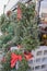 Live Christmas trees and wreaths and garlands with red bows for sale outside a store with street and cars reflected in window - se