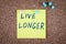 LIVE LONGER. Text on a sticky note pinned to a corkboard