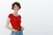 Lively attractive self-assured female trendy red t-shirt hold hands pockets stand profile turn camera smiling amused