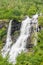 A lively Waterfall flowing down the rocks in the forest framed by trees