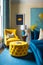 Living room with blue couch and yellow chair with blue ottoman. Generative AI