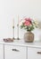 Living room interior - candles, fresh flowers in a ceramic vase,  a notebook  on a white chest of drawers in a bright scandinavian