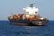 Loaded container vessel with black hull and white superstructure viewed from aft is anchoring in Mediterranean Sea.