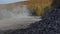 A loaded dump truck drives off along a dusty road amid a pile of stones on a clear sunny day among yellow trees. A dump truck ride