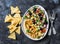 Loaded Greek salad hummus with corn tortilla chips on dark background, top view. Delicious appetizer, tapas in a mediterranean