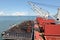 Loading coal from cargo barges onto a bulk carrier using ship cranes and grabs at the port of Muara Pantai, Indonesia. January,202