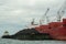 Loading coal from cargo barges onto a bulk vessel using ship cranes.