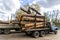 Loading heavy industrial truck trailer with big timber pine, spruce, cedar logs by crane grab loader tractor machine