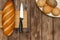 A loaf of bread on a cutting Board, buns and a knife on a wooden background
