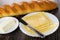 Loaf of bread, slices of cheese, knife in plate, saucer with butter on wooden table