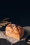 Loaf of brown bread on textile towel on dark wooden table on black background with copy space