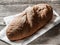 Loaf dark buckwheat bread on white textile napkin wooden table background. Fresh delicious homemade healthy bake. Bakery