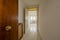 Lobby of a house with a solid wooden access door, a small corridor, white veined tiled floors and a radiator cover with grilles