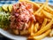 Lobster salad with french fries, salad and pickled cucumber on a white plate with blue and white table cloth