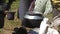 Local lady prepares tea in large metal pot on bonfire