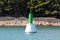 Local small green metal lighthouse warning light mounted on concrete foundation in sea next to rocky shore with dense forest