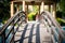 locked shot of arched wooden bridge with swimming pool on both sides with blue water and out of focus people in the