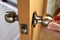 Locksmith fixes door handle rose with screw, using  screwdriver