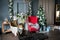 Loft-style room with a red and brown armchair, a white fireplace with flowers, decorated for Christmas. Gifts at the Christmas