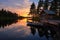 log cabin, dock, and a sailboat floating on a calm lake at sunset