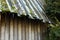 Log cabin with old roofing. Angled roof covered with green moss, snow and icicles