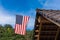 Log cabin roof & American Flag Against a Blue Sky. A red, white and blue American flag with stars and strips unfurled in the wind