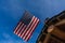 Log cabin roof & American Flag Against a Blue Sky. A red, white and blue American flag with stars and strips unfurled in the wind