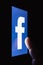 Logo of the Facebook. The finger above touch screen. The concept of dependence on popular social network