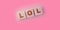 LOL abbreviation for Laughinf Out Loud on Wooden blocks on a sof pink background. Selective focus. Social concept