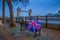 London, England - British style umbrella on a bench with iconic illuminated Tower Bridge at background