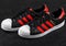 LONDON, UK - JUNE 05, 2019: Adidas Originals Superstar black shoes with red stripes on black background.German multinational