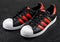 LONDON, UK - JUNE 05, 2019: Adidas Originals Superstar black shoes with red stripes on black background.German multinational