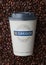 LONDON, UK - SEPTEMBER 09, 2020: Paper cup of GREGGS freshly grounded fairtrade coffee on fresh raw coffee beans