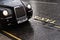 London, United Kingdom - February 01, 2019: Iconic black cab driving on the road near yellow taxi sign on wet asphalt road,